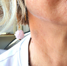 Load image into Gallery viewer, A close-up lifestyle shot of a person wearing a delicate gold dangle earring with a small, textured light pink bead charm.