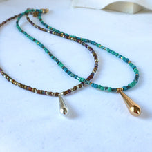 Load image into Gallery viewer, Two beaded necklaces with small faceted beads in turquoise, green, brown, and gold tones, each ending in a teardrop-shaped pendant. One pendant is silver-toned and the other is gold-toned, displayed on a light surface.