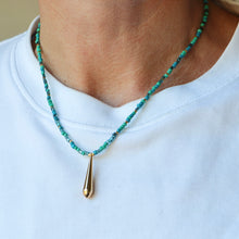 Load image into Gallery viewer, A close-up of a person wearing a beaded necklace with turquoise and green beads and a gold teardrop pendant, paired with a white crewneck shirt.