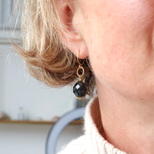 Load image into Gallery viewer, Close-up of an earring with a navy bead and gold hook on a blurred background