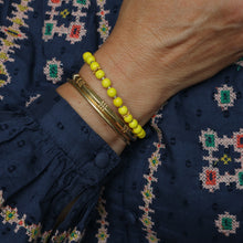 Load image into Gallery viewer, A close-up of a person's wrist wearing two bracelets: a yellow beaded bracelet and a gold-toned bangle, against a navy embroidered blouse.