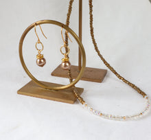 Load image into Gallery viewer, Gold-toned jewelry display with a hoop stand holding a pair of dangling earrings and a matching chain necklace draped over a white surface.