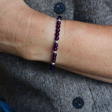 Load image into Gallery viewer, A close-up of a person's wrist wearing a beaded bracelet made of dark purple beads and small silver spacer beads, worn over a gray knit sweater.