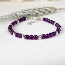Load image into Gallery viewer, A beaded sbracelet featuring deep purple amethyst round beads separated by small silver metallic spacer beads, displayed on a light textured surface with a decorative silver tassel in the background.