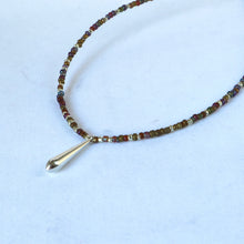 Load image into Gallery viewer, A beaded necklace with small multicolored beads and a polished gold teardrop pendant, displayed on a light blue background.