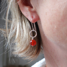 Load image into Gallery viewer, A close-up of a person's ear wearing a silver hoop earring with a dangling red glass bead.