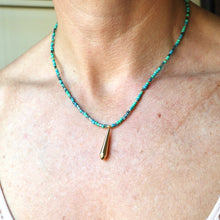 Load image into Gallery viewer, A close-up of a person's neck and chest wearing a beaded necklace with turquoise-blue beads and a small gold teardrop pendant.