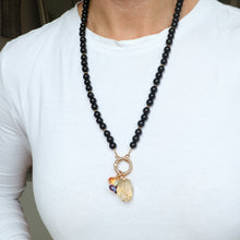 Load image into Gallery viewer, Person wearing a black beaded necklace with a gold pendant on a white shirt.