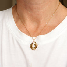 Load image into Gallery viewer, A close-up of a person wearing a delicate gold chain necklace with a sunburst flower pendant featuring a small white pearl center, styled with a white crew-neck t-shirt.