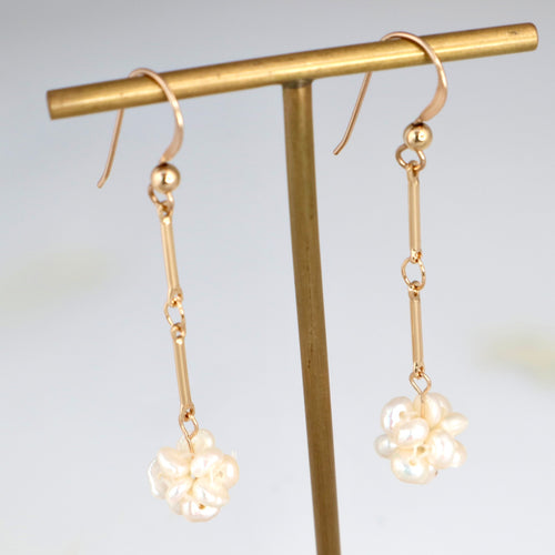 Gold earrings with floral designs hanging on a gold stand against a light background
