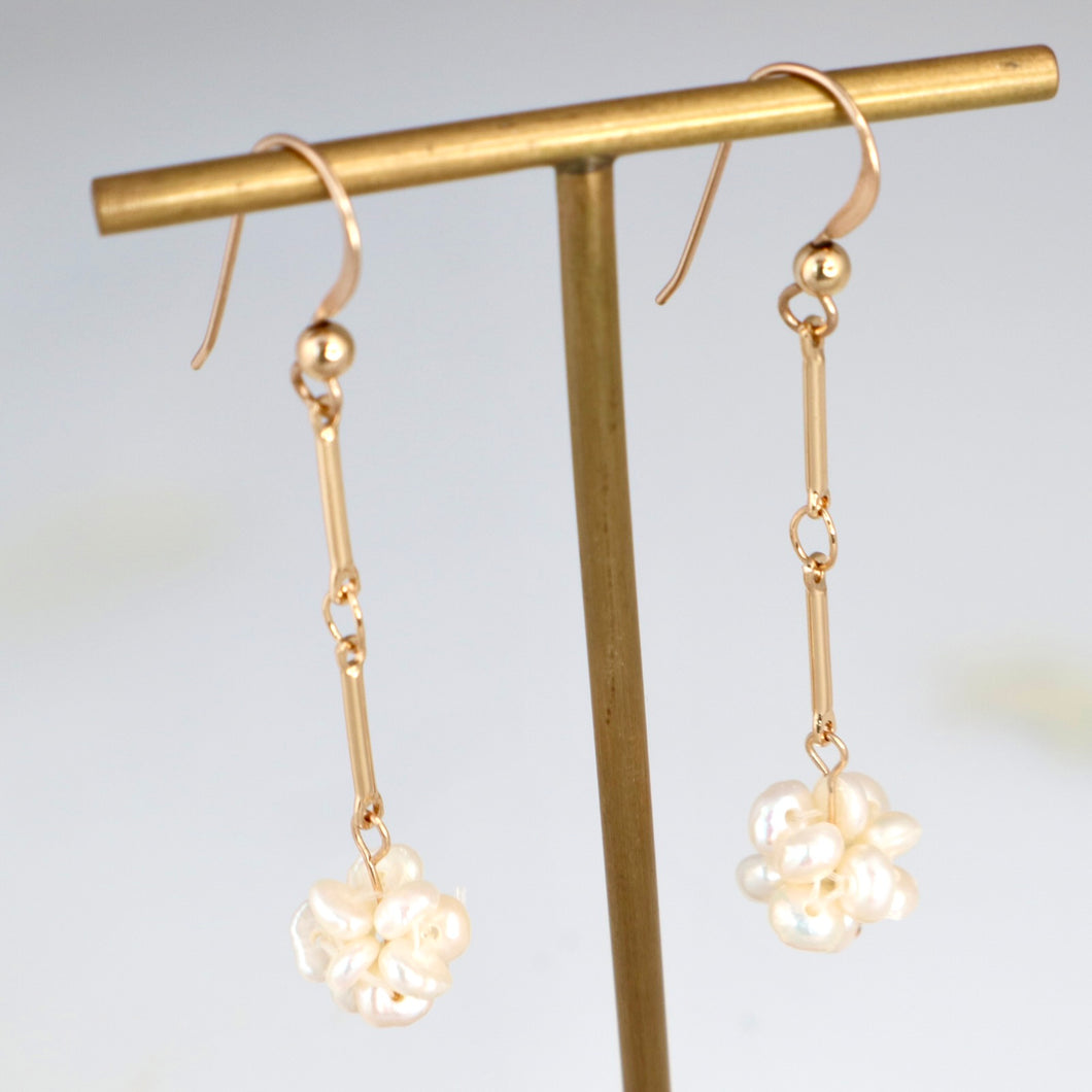 Gold earrings with floral designs hanging on a gold stand against a light background