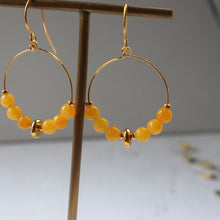 Load image into Gallery viewer, Gold hoop earrings with yellow beads on a stand against a gray background