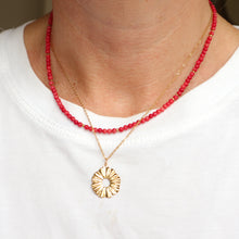 Load image into Gallery viewer, A close-up of a person's neck and chest wearing two layered necklaces: one red beaded necklace and one gold chain necklace with a textured circular pendant.