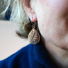 Load image into Gallery viewer, Close-up of a person wearing gold leaf-shaped earrings with a blurred background.