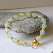 Load image into Gallery viewer, A bracelet with iridescent opaline gemstones and sparkling neon yellow beads, displayed on a rock.