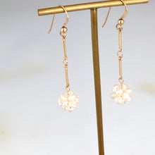 Load image into Gallery viewer, Gold earrings with floral designs hanging from a gold stand against a light background