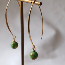 Load image into Gallery viewer, Gold hoop earrings with green spherical charms on a stand against a neutral background