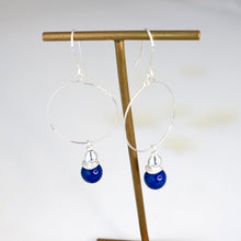 Load image into Gallery viewer, Earrings with blue drops hanging on a gold stand against a white background