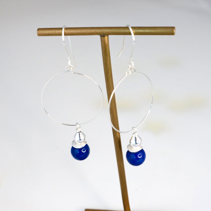 Earrings with blue drops hanging on a gold stand against a white background