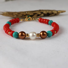 Load image into Gallery viewer, A beaded bracelet featuring red coral-like beads, turquoise blue beads, metallic bronze and white pearl-like beads, and small gold spacer beads, displayed on a light gray surface with a decorative dried leaf in the background.