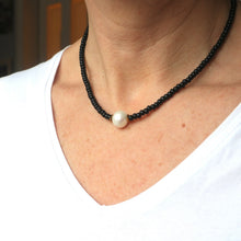 Load image into Gallery viewer, A person wearing a white v-neck t-shirt is modeling a necklace with a large freshwater pearl center and black seed bead detailing.