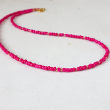 Load image into Gallery viewer, A beaded necklace made of small, round, bright pink beads separated by tiny gold spacer beads, with a gold clasp, displayed on a light off-white surface.