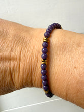 Load image into Gallery viewer, A close-up of a person's wrist wearing a beaded stretch bracelet made of purple round beads with small gold spacer accents, against a plain light background.