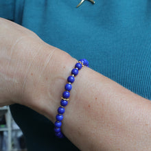 Load image into Gallery viewer, A close-up of a person's wrist wearing a beaded bracelet made of round, polished royal blue beads separated by small gold spacer rings, worn over a teal ribbed top.