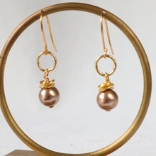 Load image into Gallery viewer, A pair of gold drop earrings with a single round pearl dangle, displayed on a gold-colored circular stand against a light gray background.