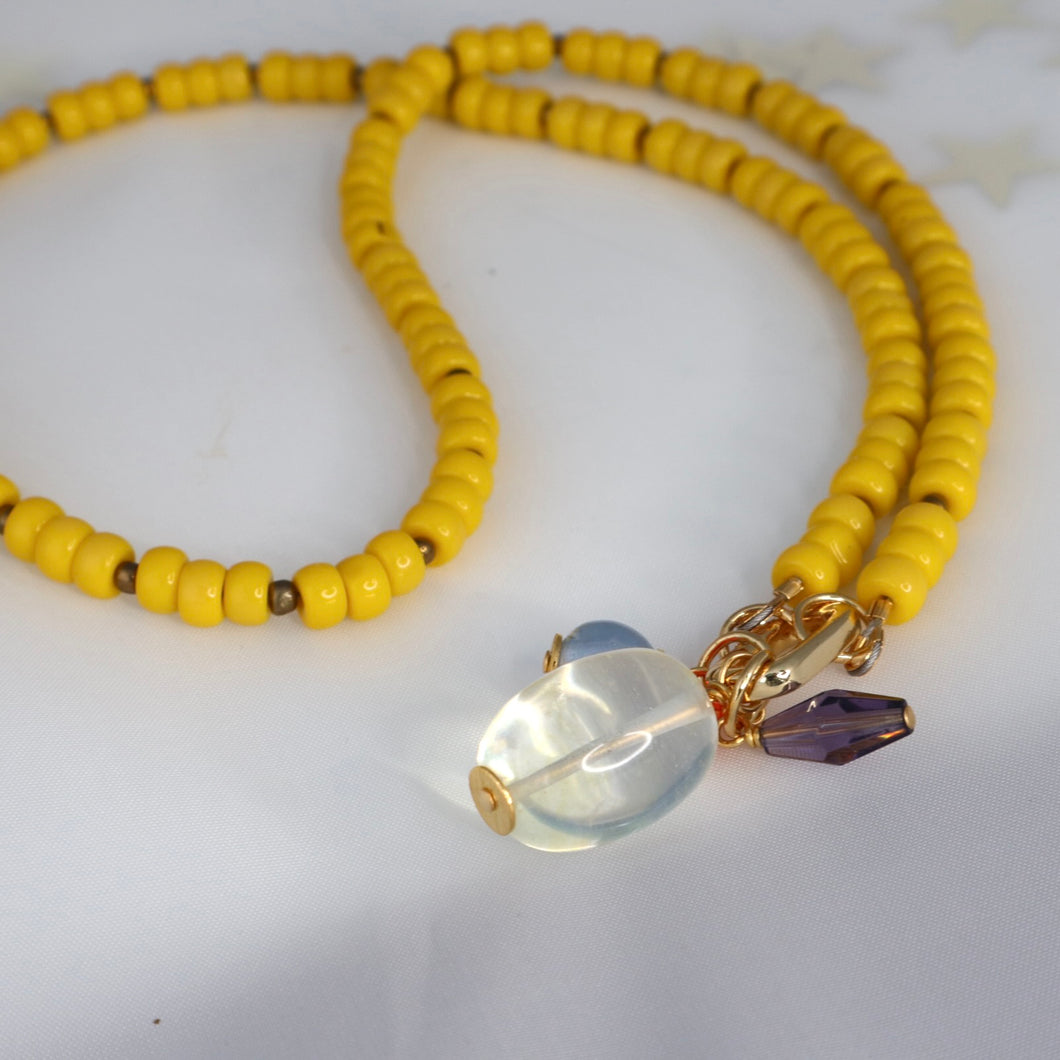 Yellow beaded necklace with a clear and purple pendant on a white background