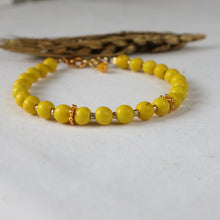 Load image into Gallery viewer, A yellow beaded bracelet with small gold spacer details, displayed on a light gray surface with a dried leaf in the background.