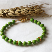 Load image into Gallery viewer, Green beaded bracelet with gold accents on a white background with wheat.