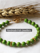 Load image into Gallery viewer, A green beaded bracelet with gold-toned accents and a gold clasp, displayed on a white surface with dried wheat stalks behind it. A text overlay reads 'Handmade Irish Jewellery'.