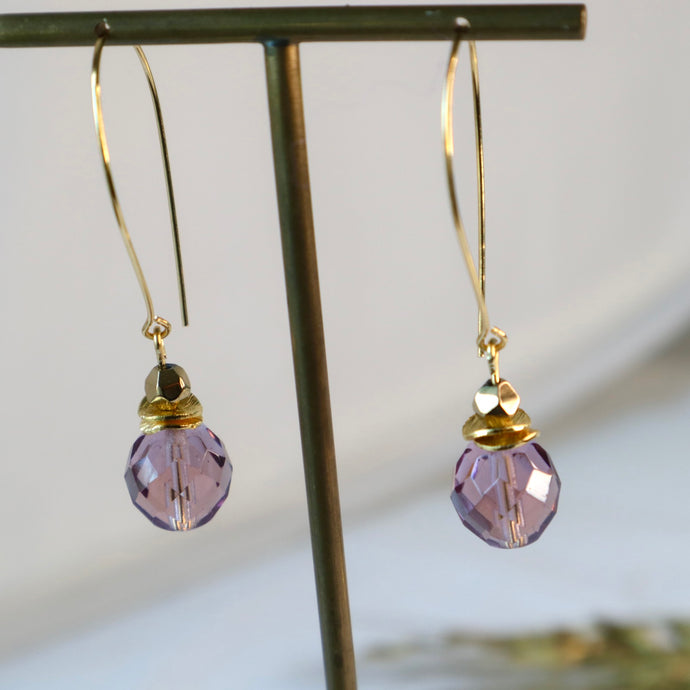 Purple beaded earrings with gold accents on a stand against a neutral background