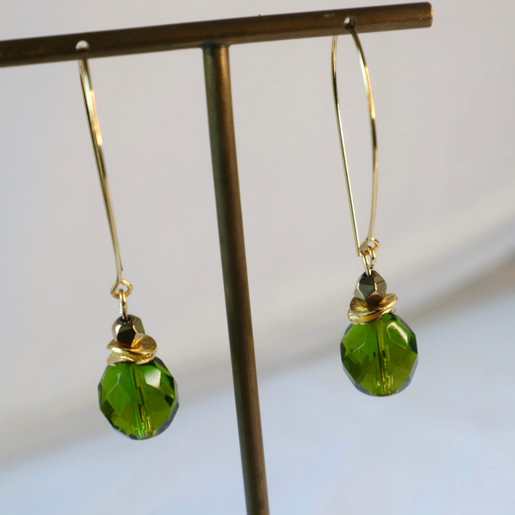 Green beaded earrings on a stand with a white background