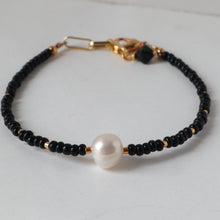 Load image into Gallery viewer, A bracelet with black seed beads and a central white pearl, accented with tiny gold tube beads and a gold plated lobster clasp.